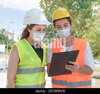 Portrait du travailleur et de l'ingénieur portant des masques de visage vérifiant le processus de production et discutant des détails du projet sur le chantier de construction. Nouvelle normale. Banque D'Images