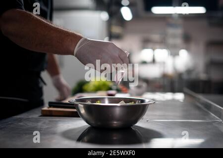 chef cuisinier mains en gants préparer la salade et ajouter du rouge oignon dans un bol dans la cuisine Banque D'Images