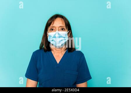 Photo de stock de professionnel de la santé portant un masque facial et un filet de cheveux jetable regardant l'appareil photo contre fond bleu. Banque D'Images