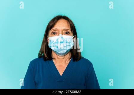 Photo de stock de professionnel de la santé portant un masque facial et un filet de cheveux jetable regardant l'appareil photo contre fond bleu. Banque D'Images