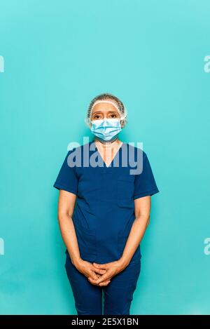 Photo de stock de professionnel de la santé portant un masque facial et un filet de cheveux jetable regardant l'appareil photo contre fond bleu. Banque D'Images