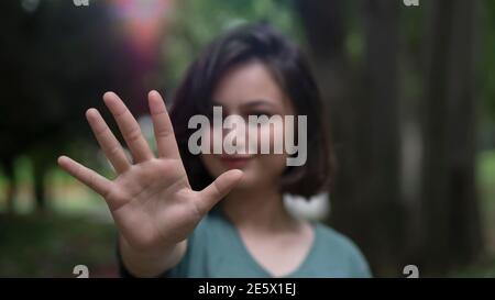 Jeune femme souriant et recrue sa main large ouverte à l'avant.Geste qui signifie arrêt montré par jeune belle femme modèle.La mise au point est à portée de main. Banque D'Images