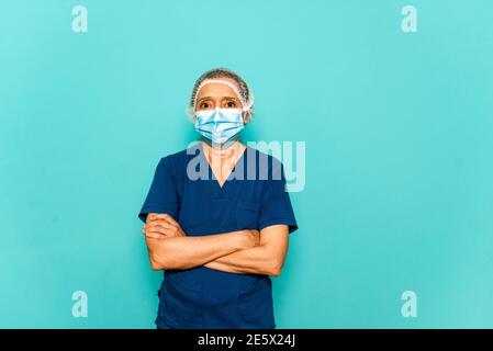 Photo de stock de professionnel de la santé portant un masque facial et un filet de cheveux jetable regardant l'appareil photo contre fond bleu. Banque D'Images