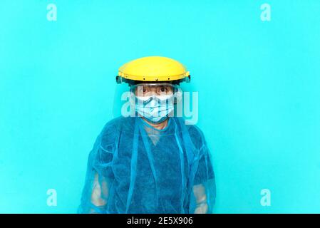 Photo d'un professionnel de santé non reconnu portant des vêtements de protection et un casque sur fond bleu. Banque D'Images