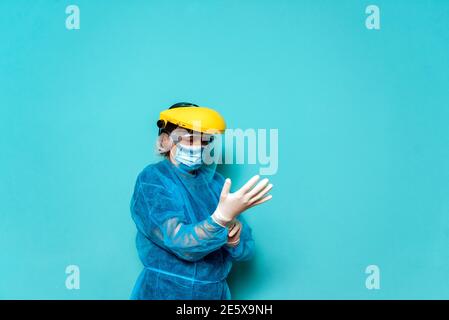 Photo d'un professionnel de santé non reconnu portant des vêtements de protection et un casque sur fond bleu. Banque D'Images