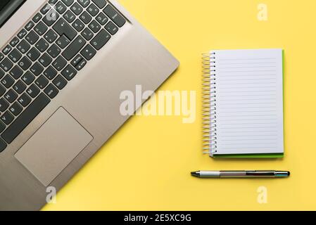 Ordinateur portable, bloc-notes en spirale et stylo sur fond jaune. Concept de bureau Banque D'Images