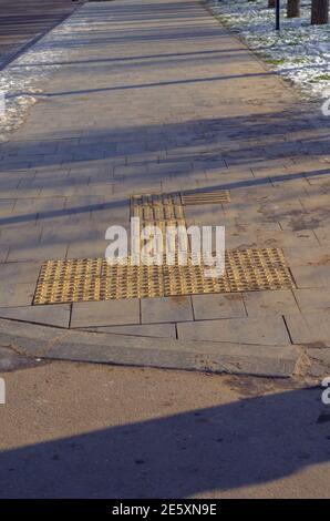 Carreaux tactiles spéciaux sur le trottoir pour les personnes ayant des problèmes de vision. Blocs en braille, carreaux pour aveugles et malvoyants. Jour d'hiver ensoleillé. Non Banque D'Images