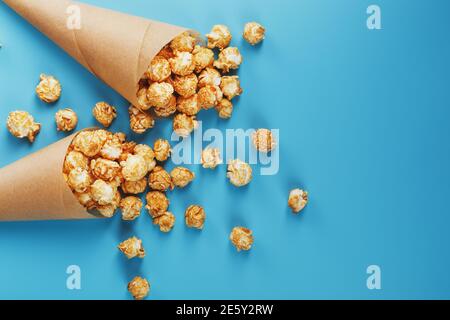 Pop-corn caramel dans une enveloppe en papier sur fond bleu. Félicitations pour avoir regardé des films, des séries, des dessins animés. Espace libre, gros plan. Minimalis Banque D'Images
