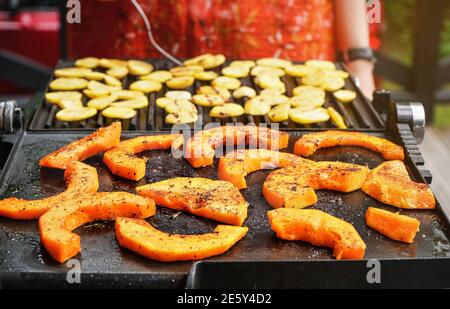 Morceaux de courge de noyer cendré orange vif assaisonnés d'épices grillées sur le gril électrique, chips de pommes de terre floues préparées en arrière-plan Banque D'Images