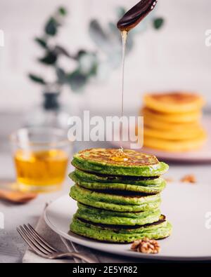 Crêpes vertes avec thé au matcha ou aux épinards, miel et raisins rouges. Petit déjeuner sain avec des superaliments. Arrière-plan clair, style scandinave élégant Banque D'Images