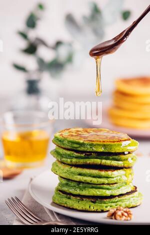 Crêpes vertes avec thé au matcha ou aux épinards, miel et raisins rouges. Petit déjeuner sain avec des superaliments. Arrière-plan clair, style scandinave élégant Banque D'Images