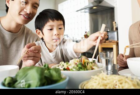 Les jeunes parents fils essaie d'utiliser des baguettes à table à manger Banque D'Images