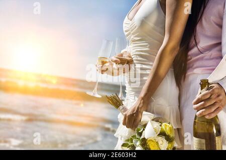 Mi-section d'un couple de jeunes mariés avec bouteille de champagne et flûtes plage Banque D'Images