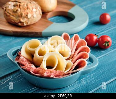 Salami italien, saucisse et fromage dans un bol en céramique. Tomates cerises. Planche à découper avec pains à grains entiers.planches en bois turquoise. Banque D'Images