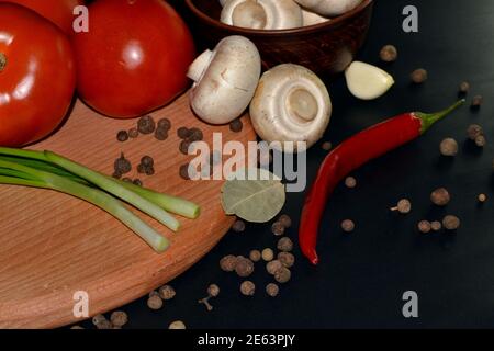 Gros plan sur les champignons frais, le piment rouge, la tomate, l'ail, la feuille de Laurier et les épices. Arrière-plan sombre Banque D'Images