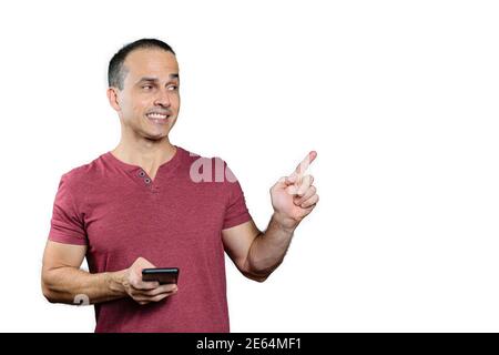 Homme brésilien mature tenant un smartphone, pointant son doigt vers la gauche et souriant. Banque D'Images