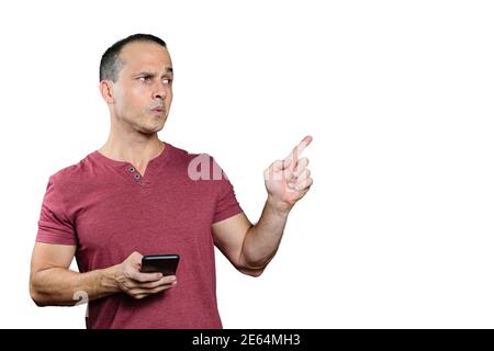 Homme brésilien mature tenant un smartphone, pointant son doigt vers la gauche et faisant un visage. Banque D'Images