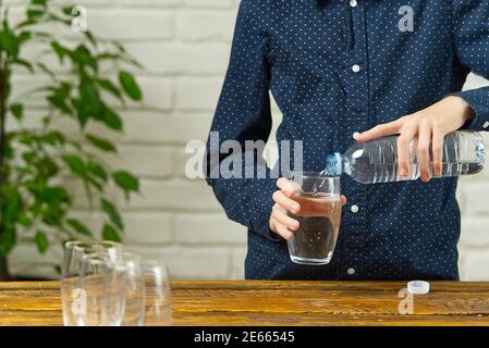 le garçon verse de l'eau de la bouteille en plastique dans le verre sur table en bois Banque D'Images