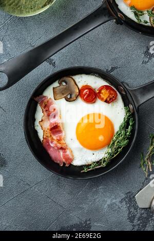 Œufs frits avec bacon et légumes dans une poêle en fonte, sur fond gris, vue de dessus plat Banque D'Images