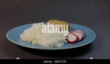Riz blanc bouilli avec côtelette de poisson enveloppée de bacon sur une assiette bleue grise. Boule de poisson avec garniture de riz et de radis. Banque D'Images