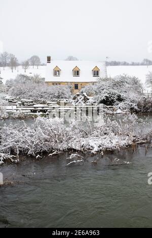 Cotswold cottage en pierre en face d'une rivière inondée windrush à Swinbrook dans la neige. Swinbrook, Cotswolds, Oxfordshire, Angleterre Banque D'Images