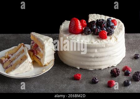 Gros plan d'un gâteau rond avec glaçage blanc crémeux et assortiment de baies utilisées comme garnitures décoratives. Servi sur fond noir gris foncé. TW Banque D'Images