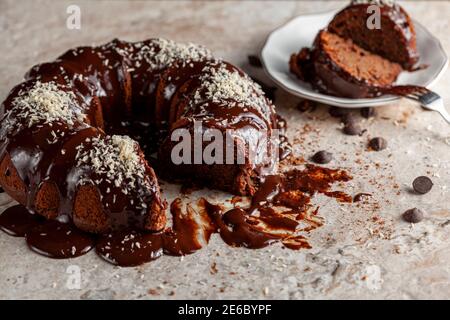 Vue latérale inclinée d'un gâteau au chocolat rond gastronomique avec des noix de coco râlées sur la glace. Deux tranches ont été retirées et placées sur une plaque en porcelaine blanche avec un moi Banque D'Images