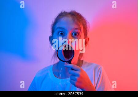 Une jolie petite fille regarde à travers une loupe. Le concept d'une enfance heureuse, de la science et de l'éducation d'un enfant dans la famille. Isolé sur whi Banque D'Images