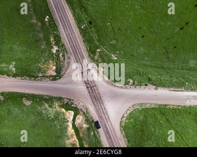 Vue aérienne en hauteur de l'intersection de deux routes rurales de campagne entre les prairies vertes. Une voiture solitaire est garée sur le côté de la route Banque D'Images