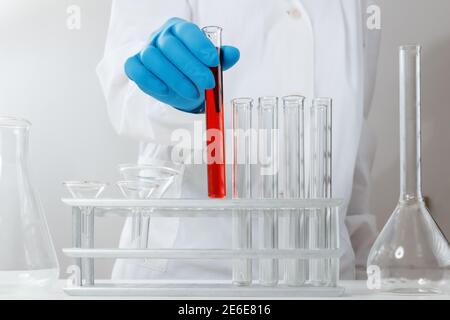 Dans un laboratoire chimique, un pharmacien analyse un tube à essai avec du liquide rouge. Expérience médicale. Un chimiste travaille sur un test avec la protection gl Banque D'Images