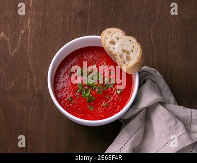 Délicieuse soupe végétalienne de tomates cuites au four et de poivrons avec herbes dans une assiette blanche sur un fond de bois, vue du dessus Banque D'Images