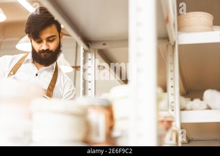 Jeune homme d'affaires séduisant un potter avec une barbe et une moustache travaille dans son atelier. Conserve les enregistrements et transcrites dans un ordinateur portable en inspectant Banque D'Images