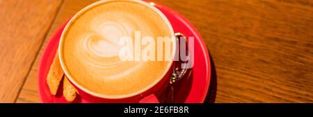 Latte Art, vue latérale du café chaud isolé sur fond de bois. Le matin avec une tasse de café ou de cappuccino rouge. Café d'art et d'artisanat. Bannière web Banque D'Images