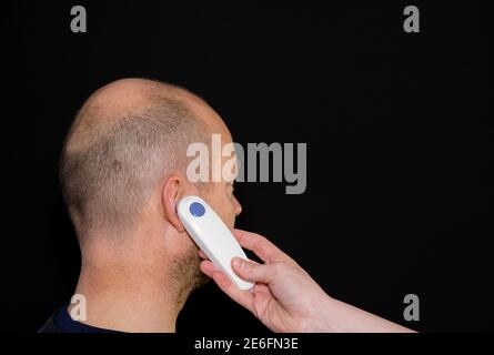 Homme adulte ayant sa prise de température avec un thermomètre auriculaire numérique. Banque D'Images