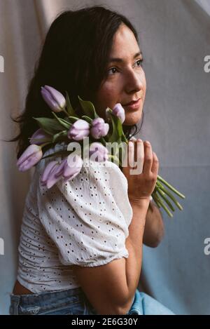 portrait authentique de la jeune femme en vêtements décontractés tenant des tulipes violettes, lumière naturelle douce. concept de féminité. personnes authentiques, rêvant et t Banque D'Images