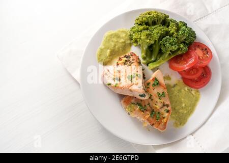 Repas diététique sain à faible teneur en glucides avec filet de thon frit, brocoli, tomates, persil et sauce aux herbes de citron sur une assiette blanche et une table en bois clair, Copy sp Banque D'Images