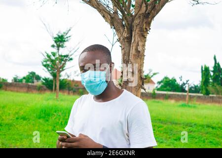jeune homme noir portant un masque nasal, assis et utilisant son smartphone Banque D'Images