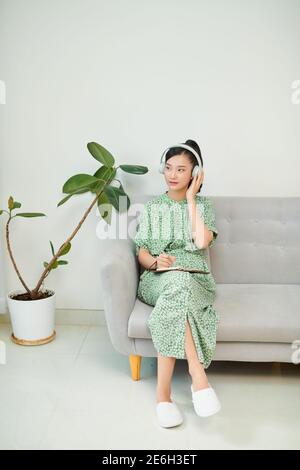 Une jeune femme asiatique écoute de la musique à partir d'écouteurs et écrit une note pour son idée de travail dans un livre de journal. Banque D'Images