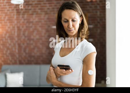 Femme qui teste le niveau de glucose avec un moniteur de glucose continu sur mobile Téléphone Banque D'Images