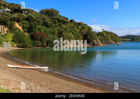 Baie d'Opito dans la baie des îles, Nouvelle-Zélande/ UN kayak repose sur la plage de sable et les arbres pohutukawa fleurissent sur la rive Banque D'Images