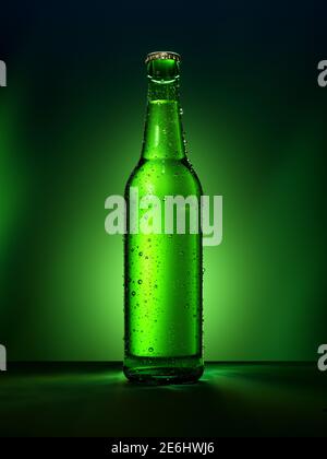 Une seule bouteille de bière verte sans désignation de marque. Bouteille en verre pleine recouverte de gouttes d'eau sur fond vert éclairé. Boissons alcoolisées Banque D'Images