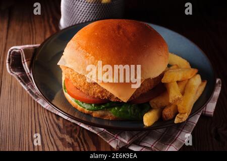 Filet de poulet dans un pain de brioche avec laitue tomates, fromage et peau sur des frites tournées avec créativité éclairage Banque D'Images