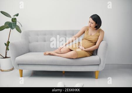 Femme enceinte massant un pied gonflé. Enflure pendant la grossesse. Jambes gonflées. Femme enceinte assise sur le canapé. Banque D'Images
