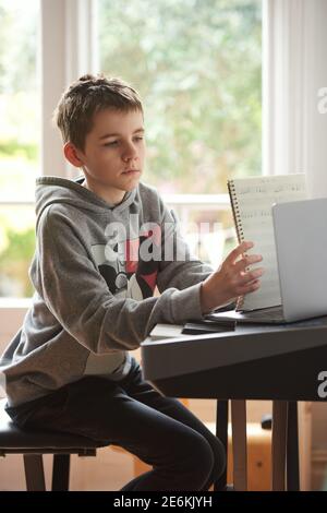 Adolescent ayant une leçon de piano à distance en ligne. Il montre son travail à l'enseignant en le tenant jusqu'à l'ordinateur portable. Banque D'Images