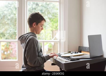 Adolescent ayant une leçon de piano à distance en ligne. Il joue un clavier de piano avec un ordinateur portable ouvert. Banque D'Images