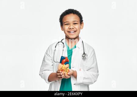 Enfant afro-américain pendant l'apprentissage de l'anatomie humaine, tient un modèle anatomique de coeur, pour étudier la structure du corps. Isolé sur blanc Banque D'Images