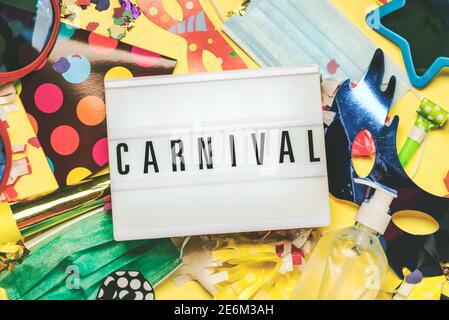 Concept de carnaval pendant le covid-19.Lightbox avec le mot Carnaval, à côté de masques chirurgicaux protecteurs, masque de carnaval et bouteille d'assainisseur sur jaune Banque D'Images