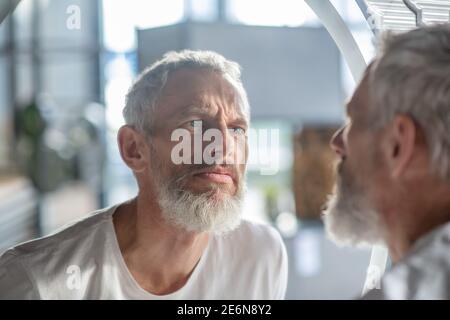 Homme à poil gris barbu regardant le miroir Banque D'Images