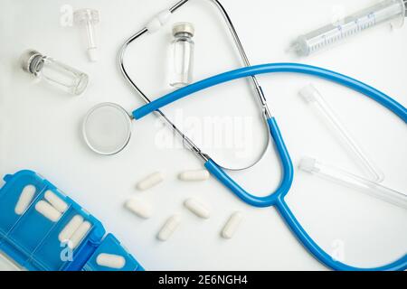 Mise en page médicale sur fond blanc, sur fond plat. Stéthoscope ou phonendoscope bleu entouré de capsules, d'ampoules et de tubes à essai. Banque D'Images