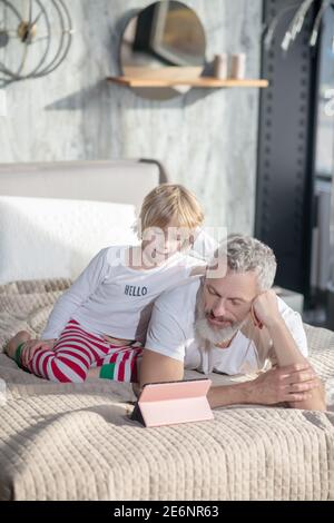 Bébé assis papa couché regardant la tablette Banque D'Images